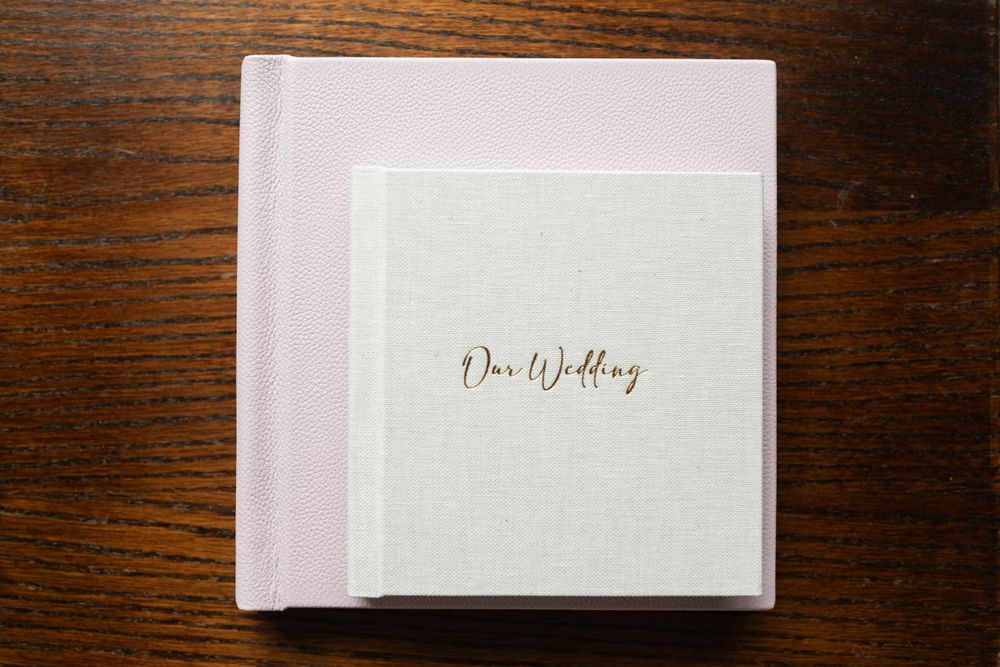 Wedding album with gold lettering on white textured cover in a light pink box.
