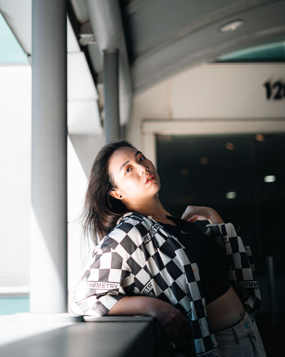 Dramatic indoor portrait with checkered pattern clothing against an architectural background.