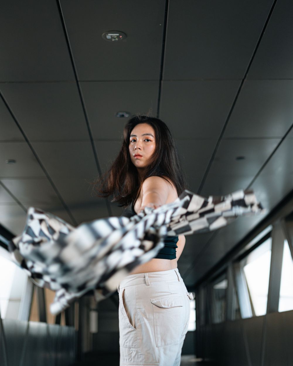 Modern fashion portrait with flowing checkered jacket in an industrial corridor.