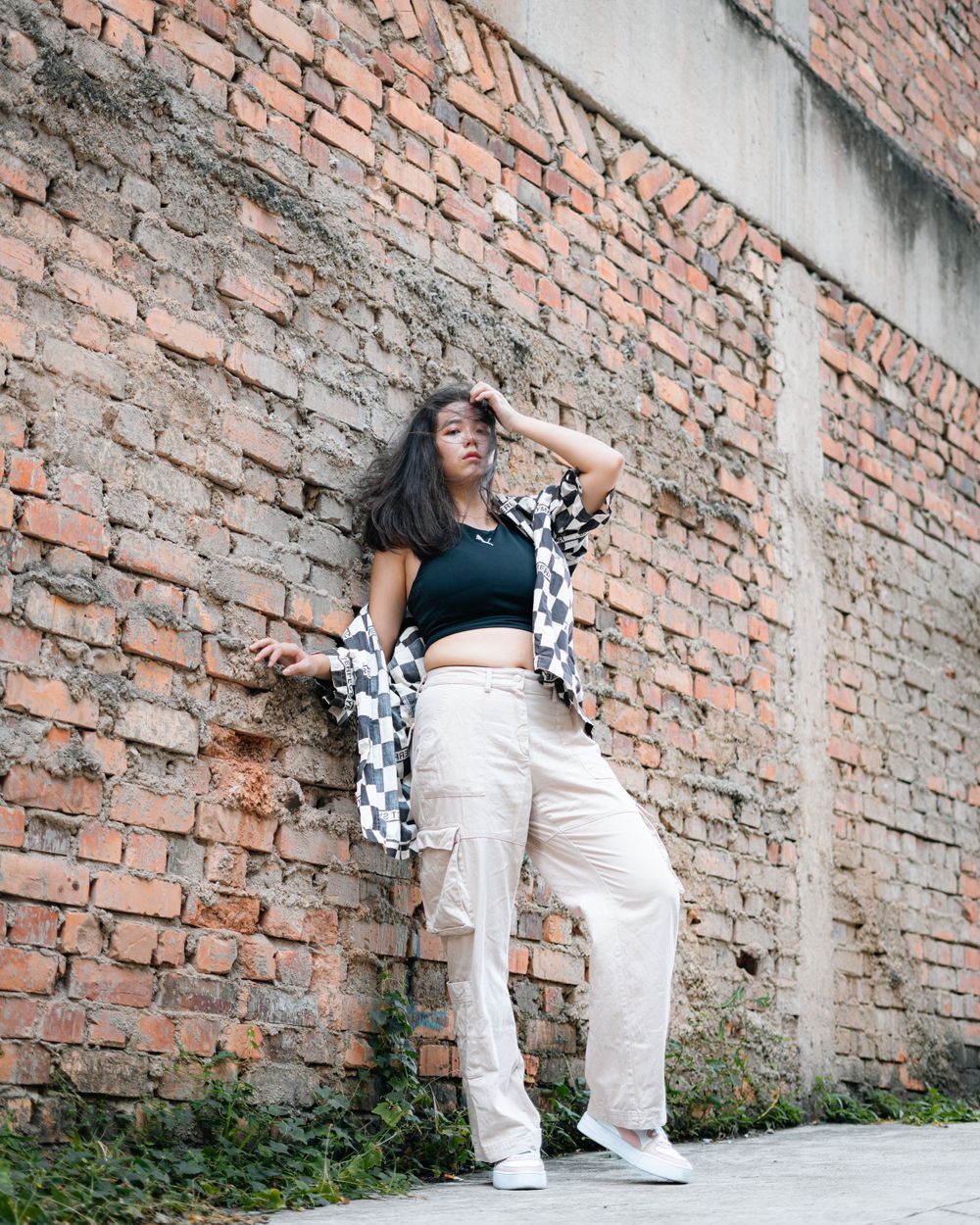 Street style portrait against rustic brick wall wearing black crop top and checkered pattern jacket.