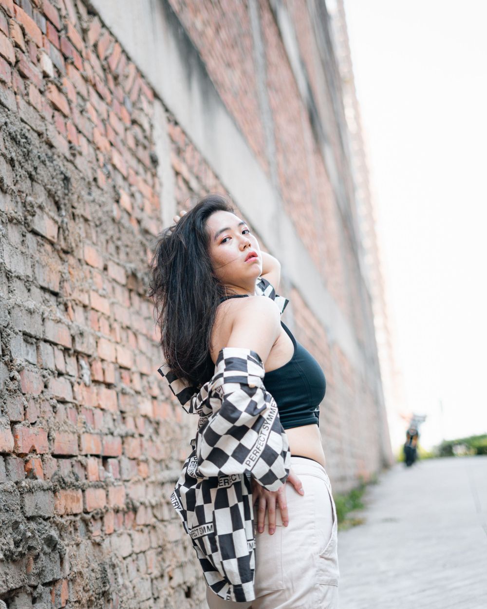 Fashion portrait against weathered brick wall featuring black and white checkered outerwear.