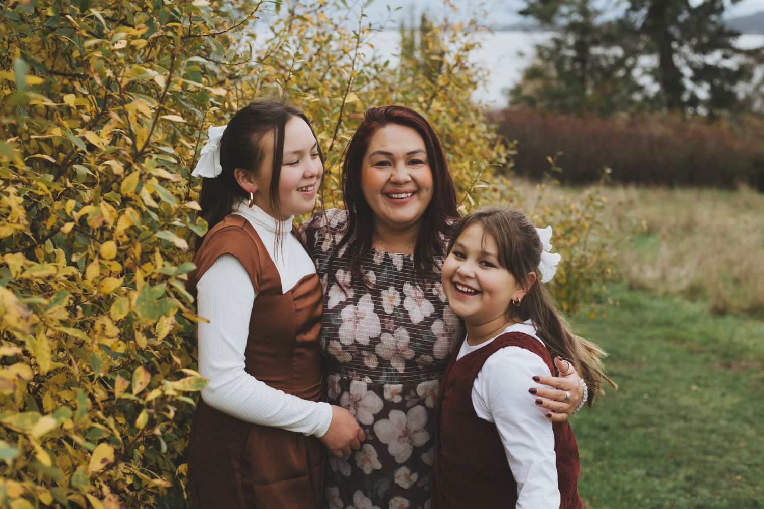 Three people sharing warm embraces and laughter against autumn foliage.