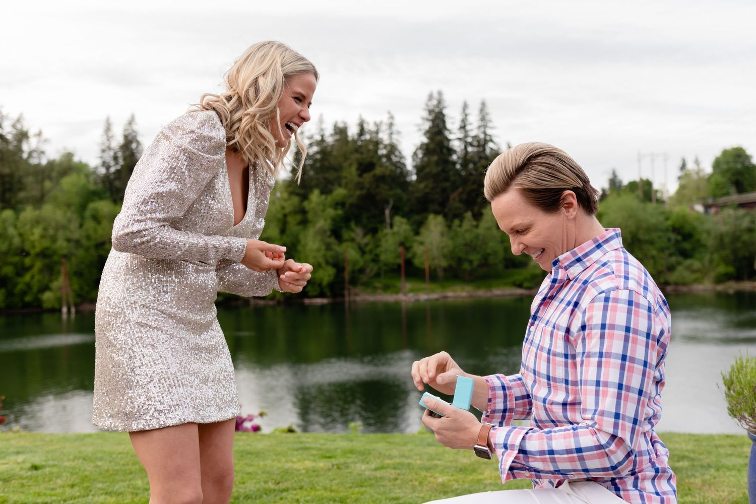 Couple sharing an emotional moment during lakeside proposal surrounded by evergreen trees.