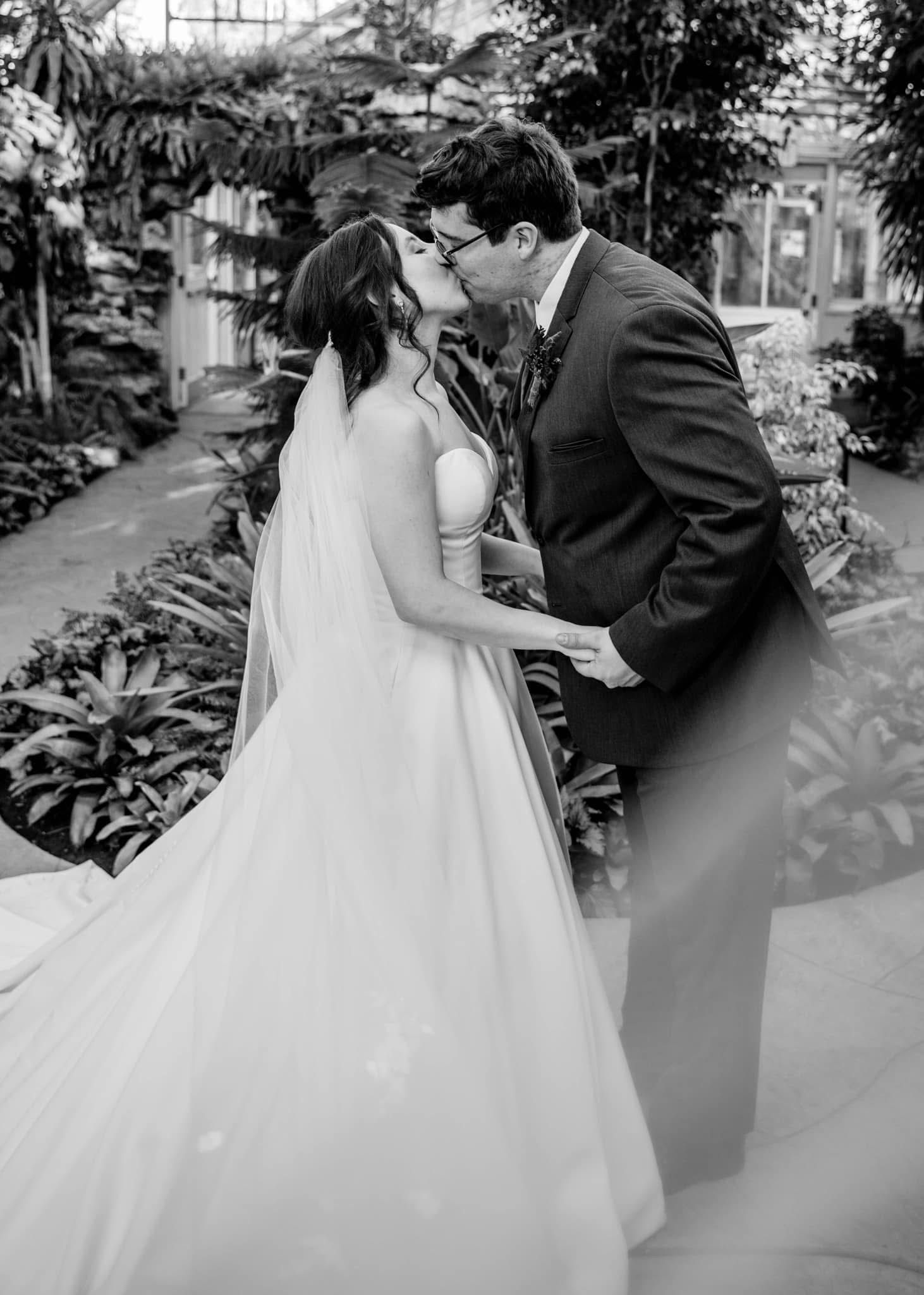A romantic black and white photo of a bride and groom sharing a tender moment in a garden setting.