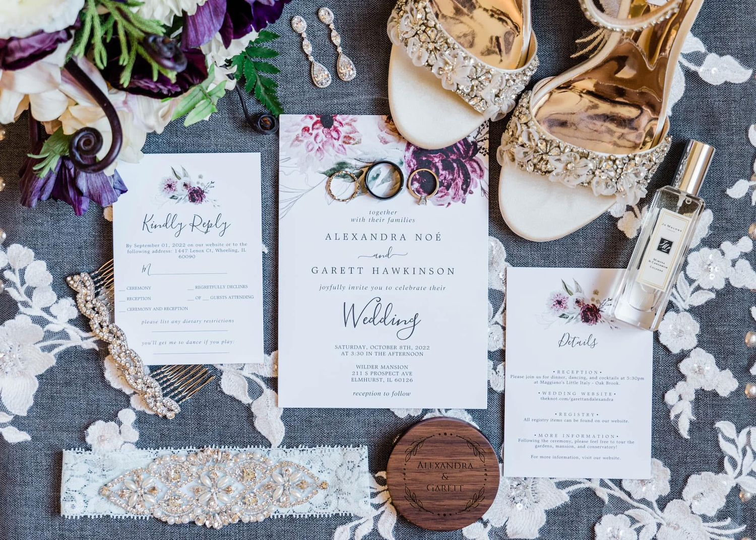 Wedding stationery flatlay with invitations, rings, and decorative floral elements on a textured gray background.