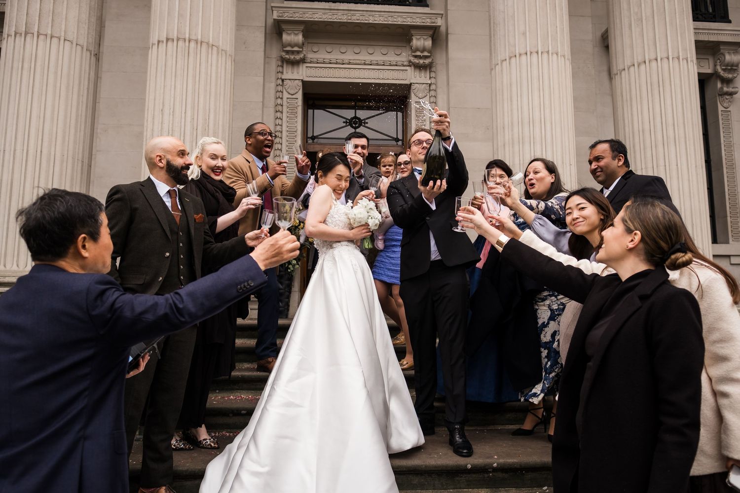 Wedding celebration on grand stone steps as guests joyfully toss flower petals at the newlywed couple.