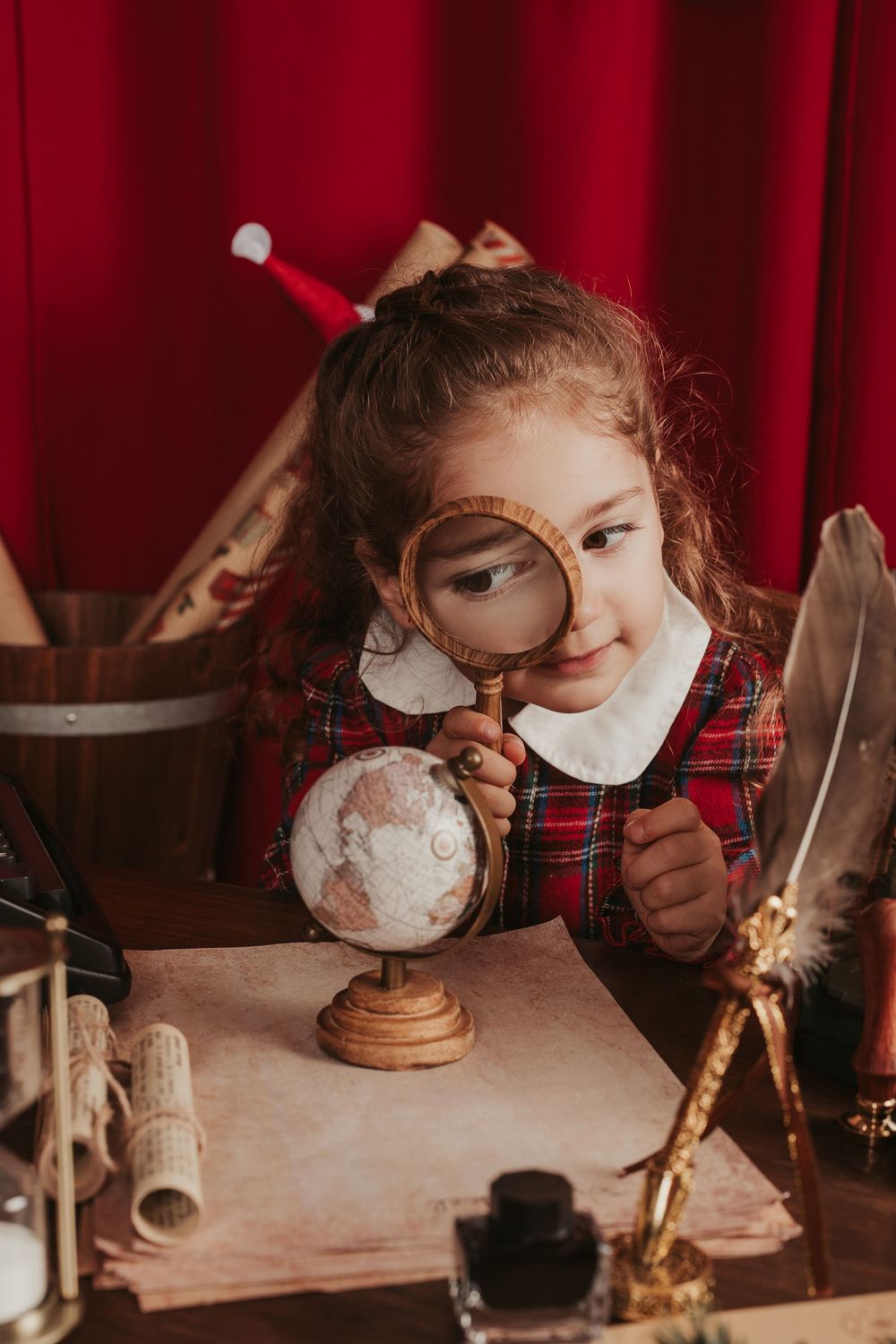 Child in plaid shirt wearing protective mask works intently at wooden desk with art supplies and materials.