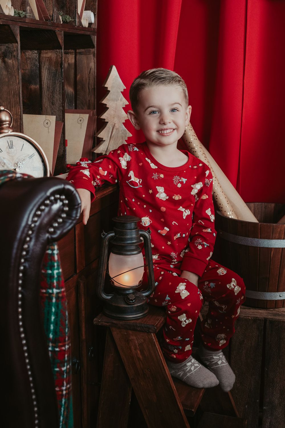 A festive holiday photo setup with red curtains, wooden barrels, and lantern decorations against a rustic backdrop.