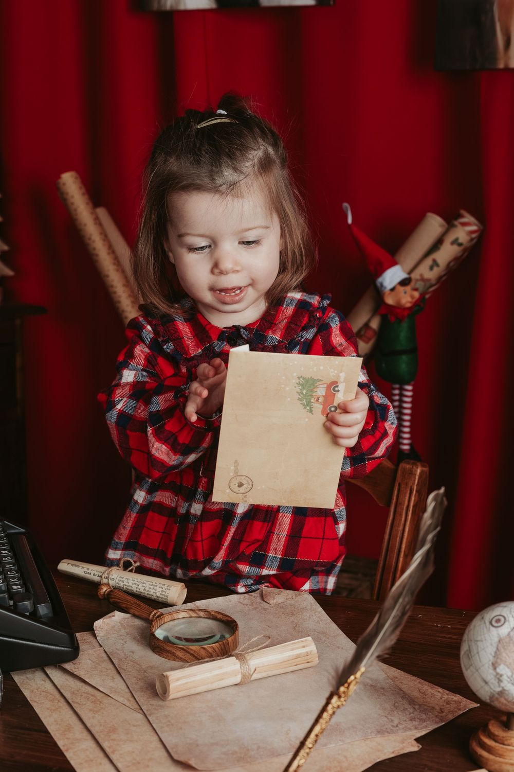 A small child in a red plaid shirt works at a wooden table with craft materials and tools.