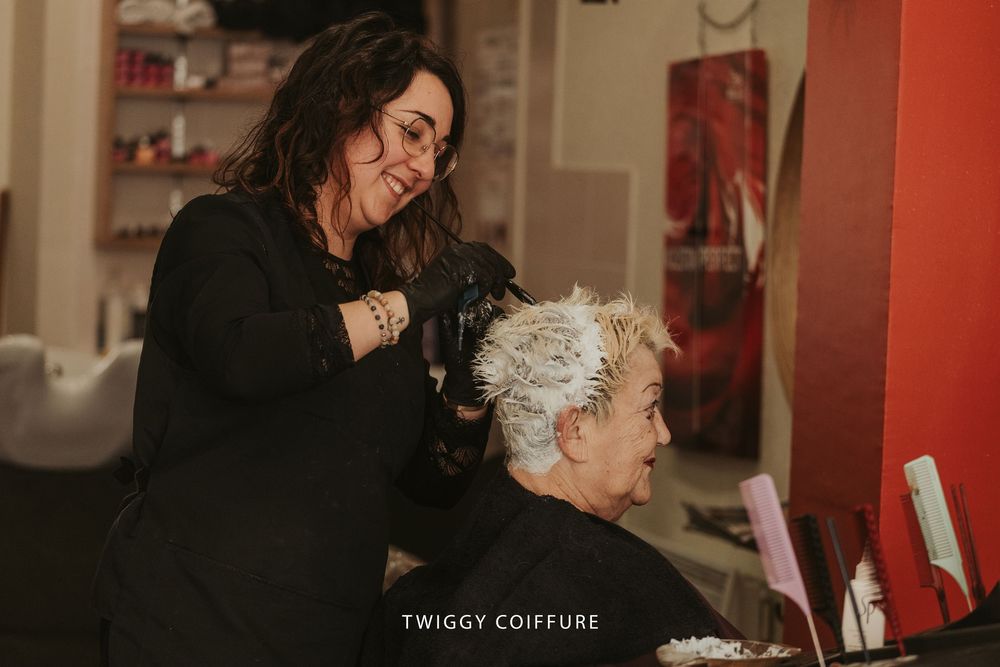 Hair stylist in black top styling client's platinum blonde hair at Twiggy Coiffure salon.