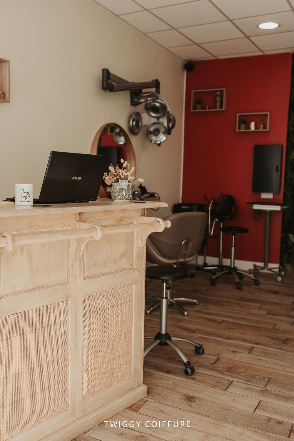 Interior view of a modern hair salon with wooden reception desk and red accent wall showing multiple styling stations.