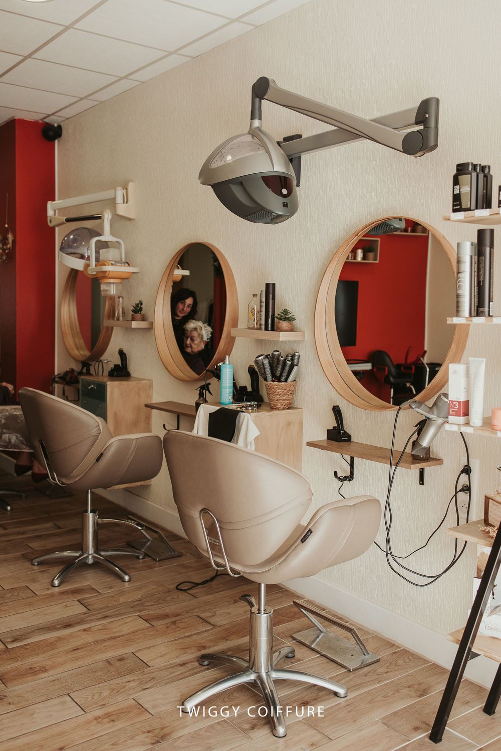 Modern hair salon interior with white styling chairs and round mirrors mounted on beige and red accent walls.