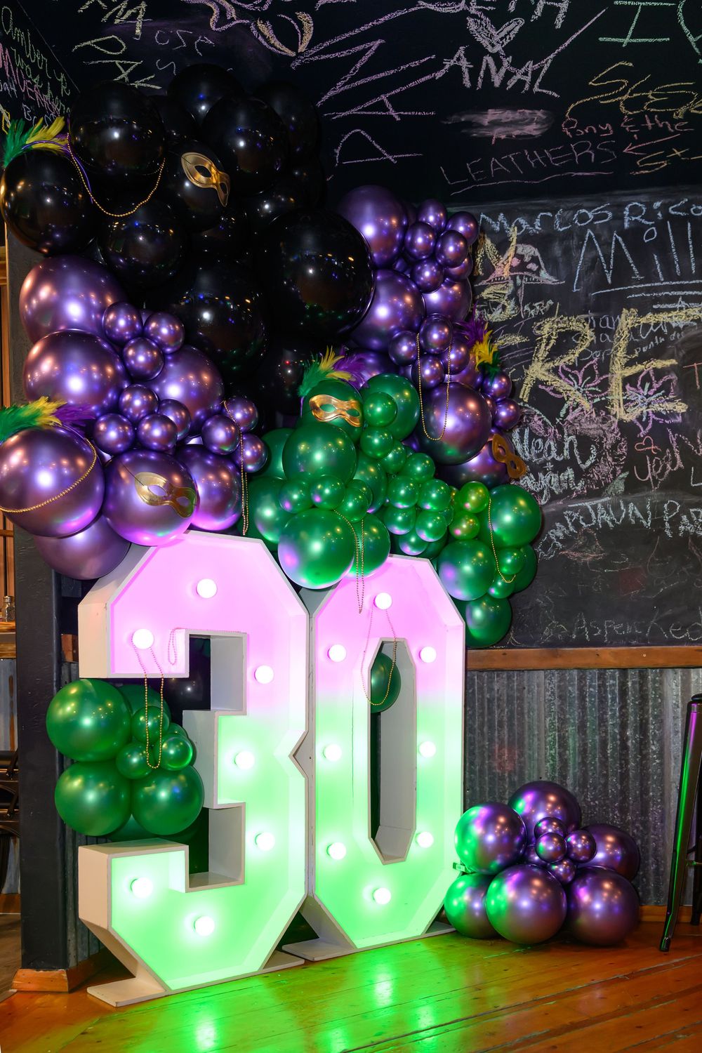 Illuminated 30th birthday marquee sign surrounded by purple and green balloon arch display.