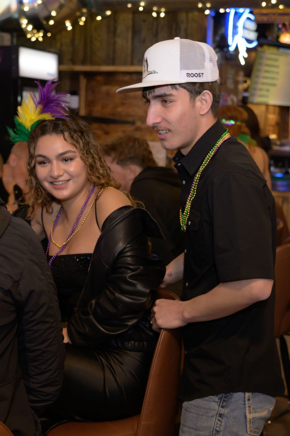 A young couple at a Mardi Gras party, woman in leather outfit with feather headband, man in white cap with beads.