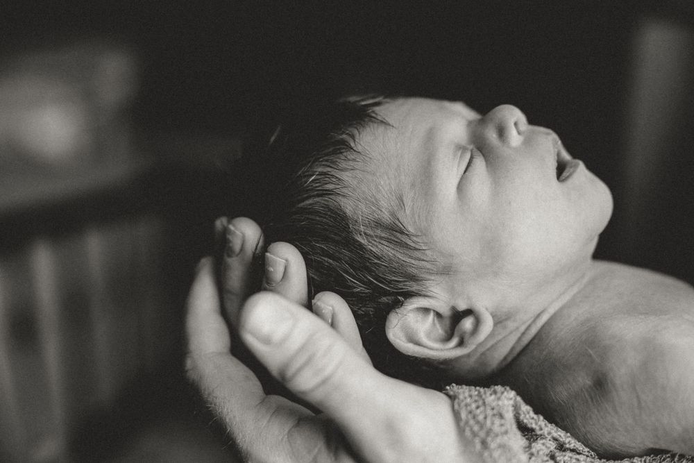 A close-up black and white photo of a peaceful sleeping infant resting in gentle hands.