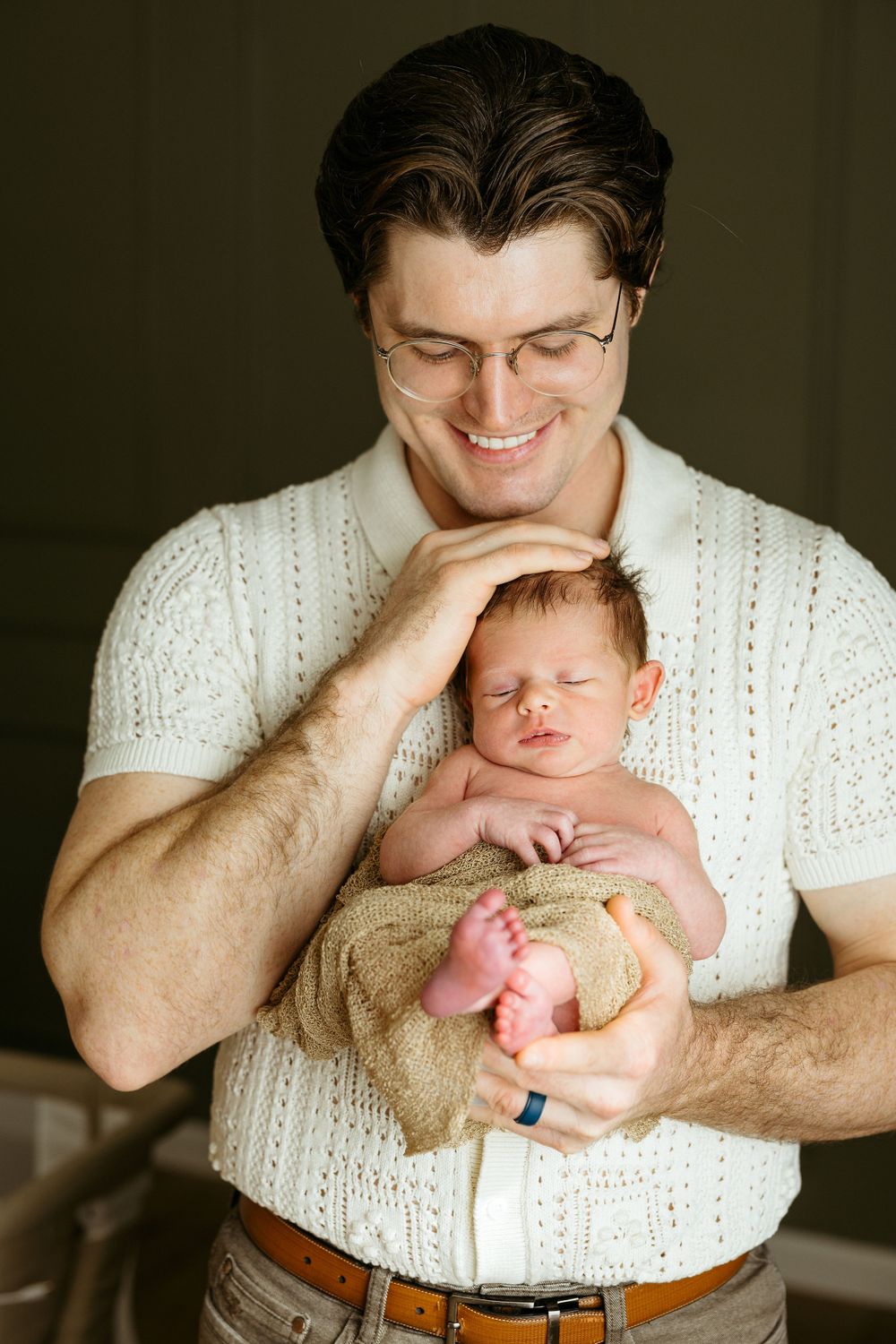 A tender moment between parent and sleeping newborn baby wrapped in a brown blanket.
