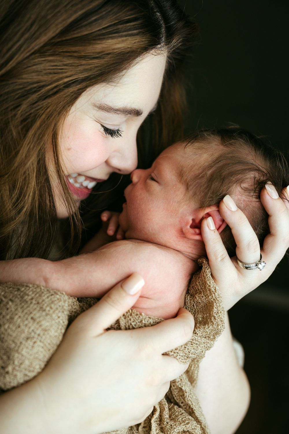 A tender moment shows a newborn baby being cradled closely while wrapped in a soft brown blanket.
