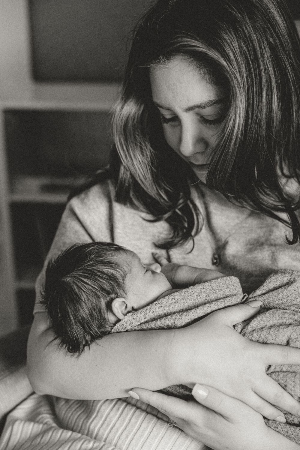 A tender black and white portrait captures an intimate bonding moment between parent and baby wrapped in blankets.