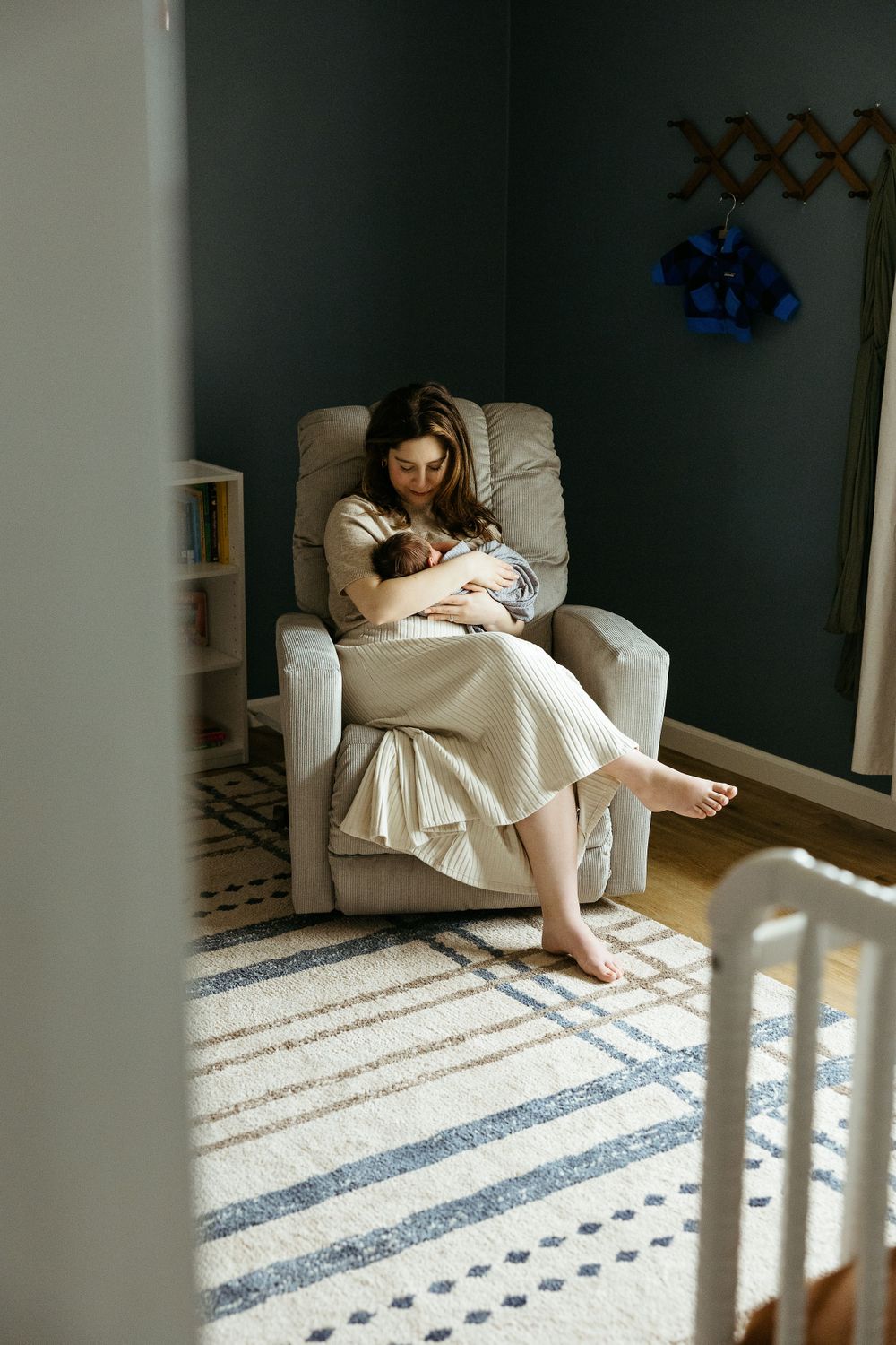 A cozy nursery scene with a comfortable recliner, striped area rug, and natural light streaming through the window.