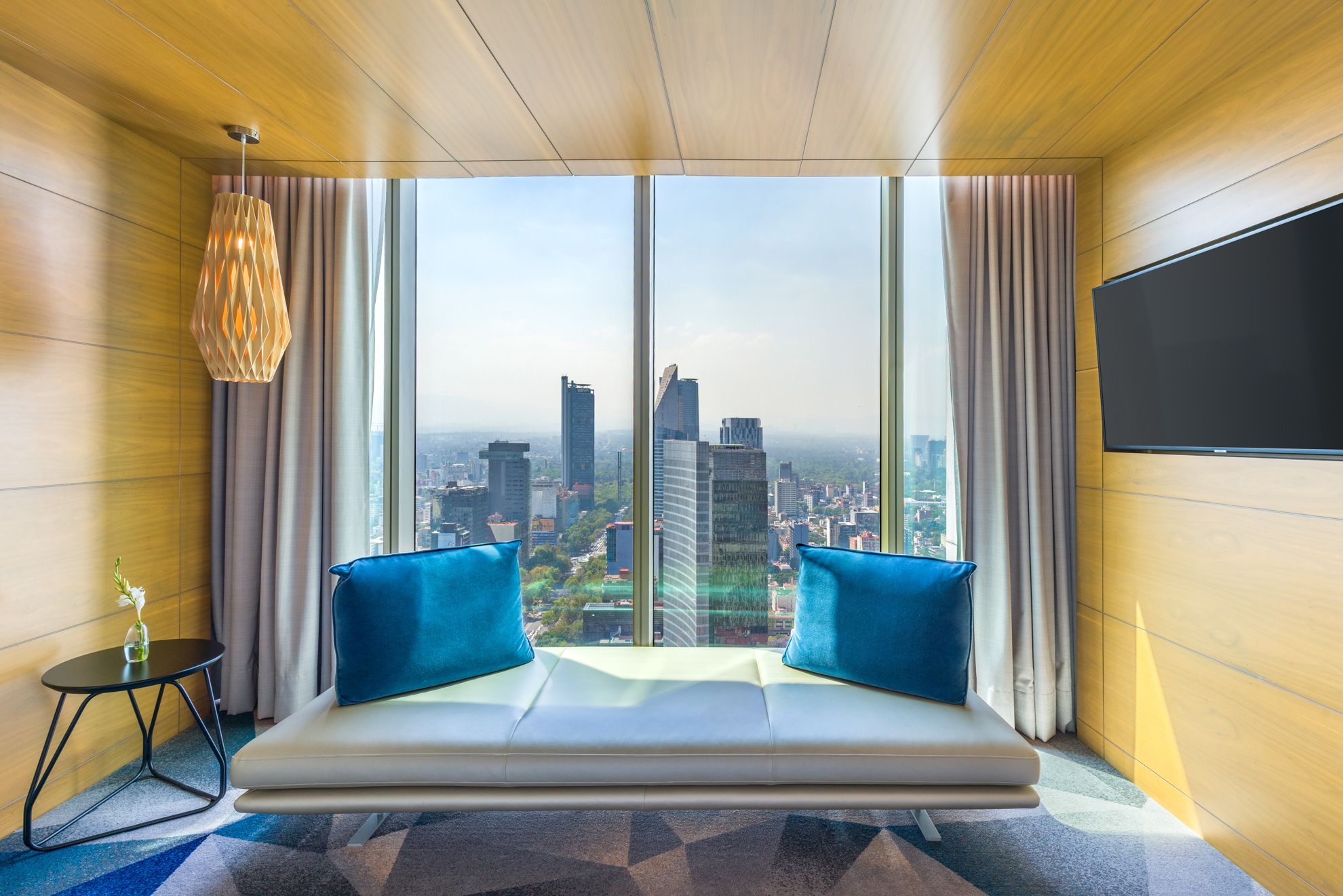 Indoor luxury swimming pool with wooden deck and geometric wall patterns overlooking city views. Sofitel Mexico City Reforma.
