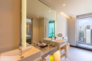 Modern luxury hotel bathroom with marble vanity, twin sinks, and city views through floor-to-ceiling windows.