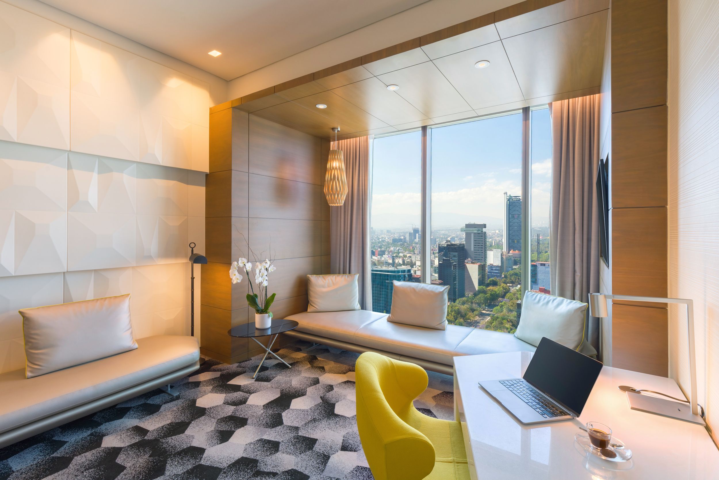 Modern luxury hotel room with floor-to-ceiling windows, yellow accent chair, and panoramic city views.