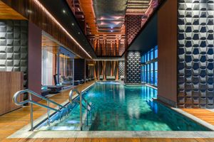 Indoor luxury swimming pool with wooden deck and geometric wall patterns overlooking city views. Sofitel Mexico City Reforma.