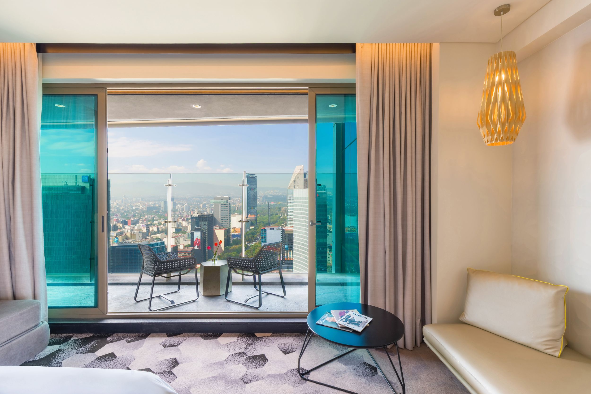 Luxury hotel room with floor-to-ceiling windows offering panoramic city views of Bangkok, featuring modern furnishings and decor.