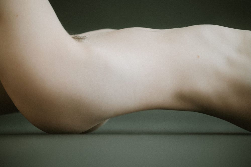 Artistic close-up of a nude torso silhouette against dark background showcasing curves and shadows.