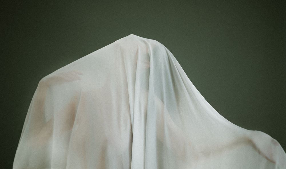 Ethereal white fabric draped against a dark green background creates a ghostly sculptural form.