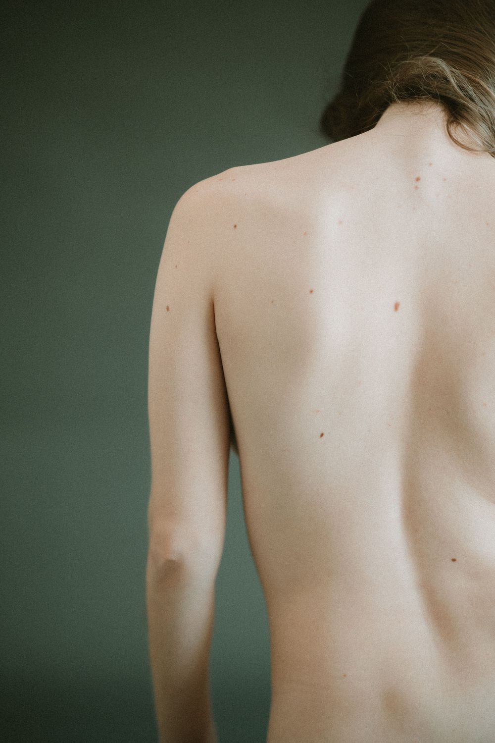Close-up artistic photograph of a bare back against dark background showing smooth pale skin and subtle body contours.
