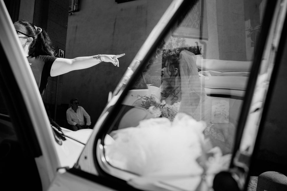 A black and white photo of a person reclining inside a car, viewed through the car window.