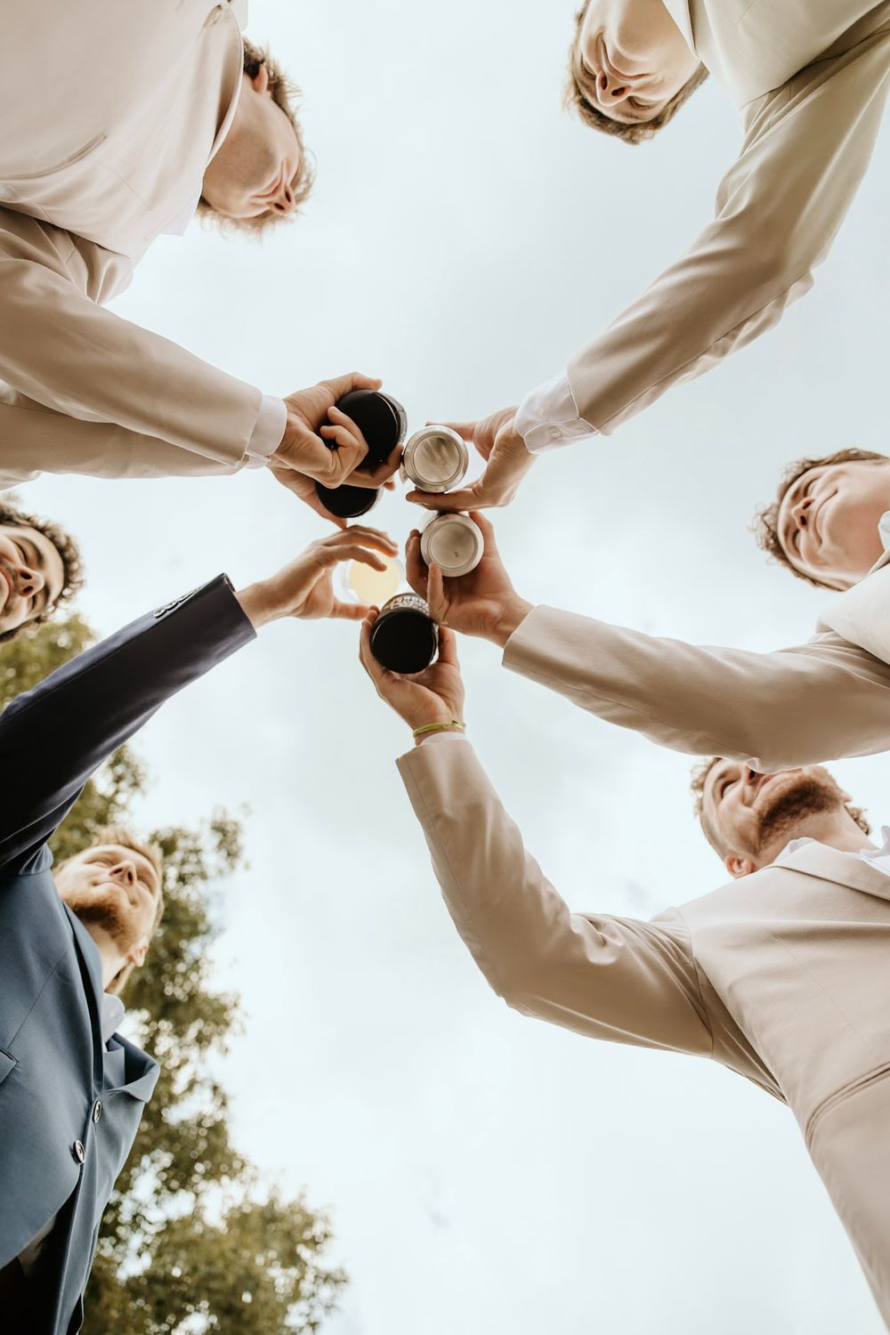 Low angle view of people toasting with wine and champagne glasses against bright sky in celebratory moment.