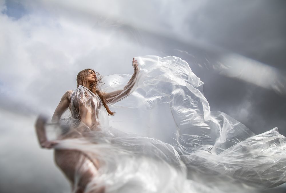 A woman in flowing white fabric dances dramatically against a stormy sky, her dress billowing in the wind.
