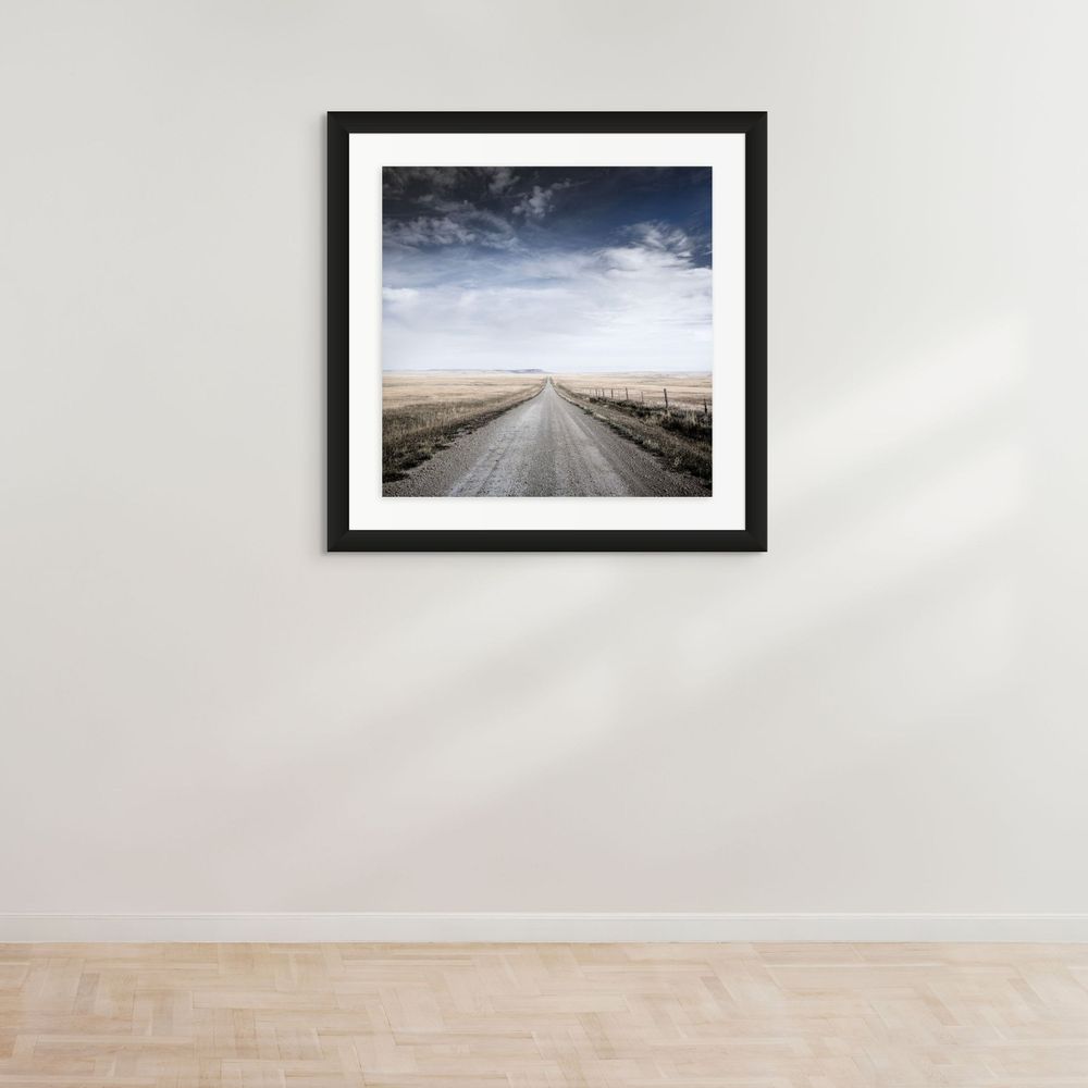 Empty rural dirt road stretching into the distance under dramatic storm clouds.