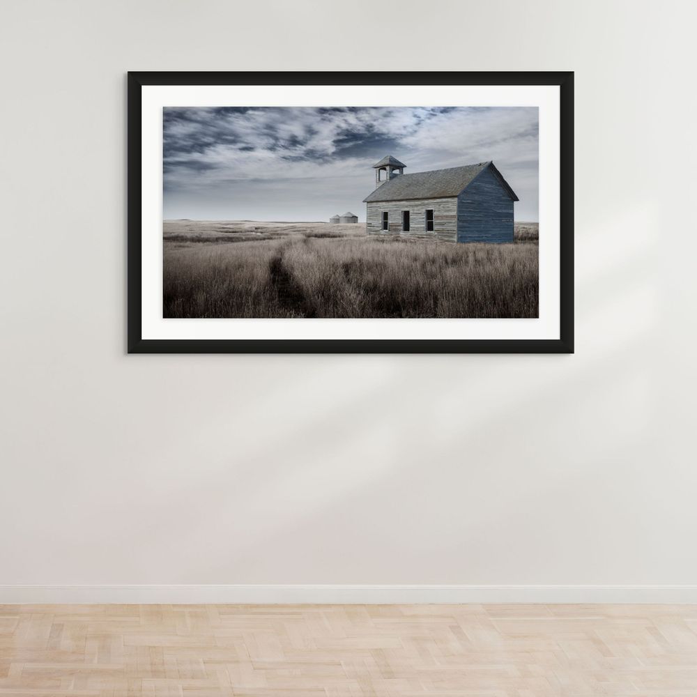 Lone white schoolhouse standing in prairie grass under moody sky.
