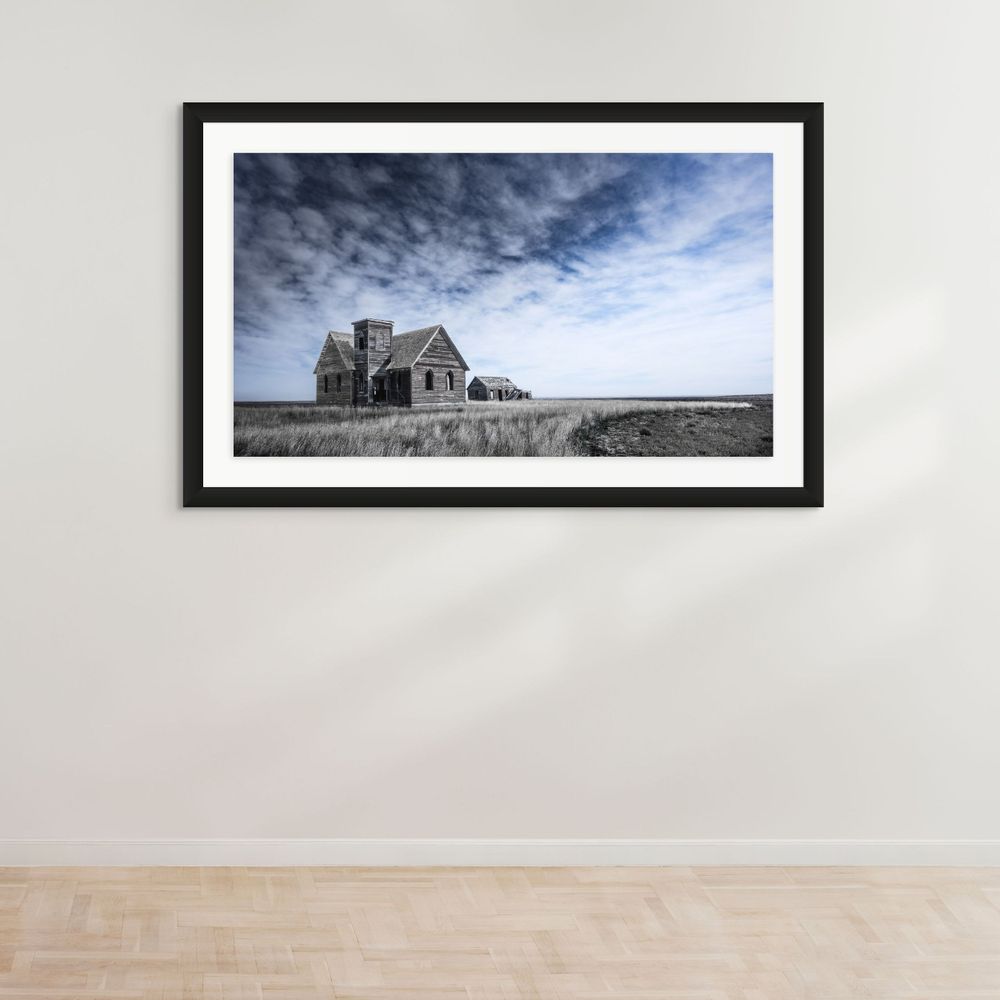 Abandoned farmhouse and outbuildings on prairie landscape beneath cloudy skies.
