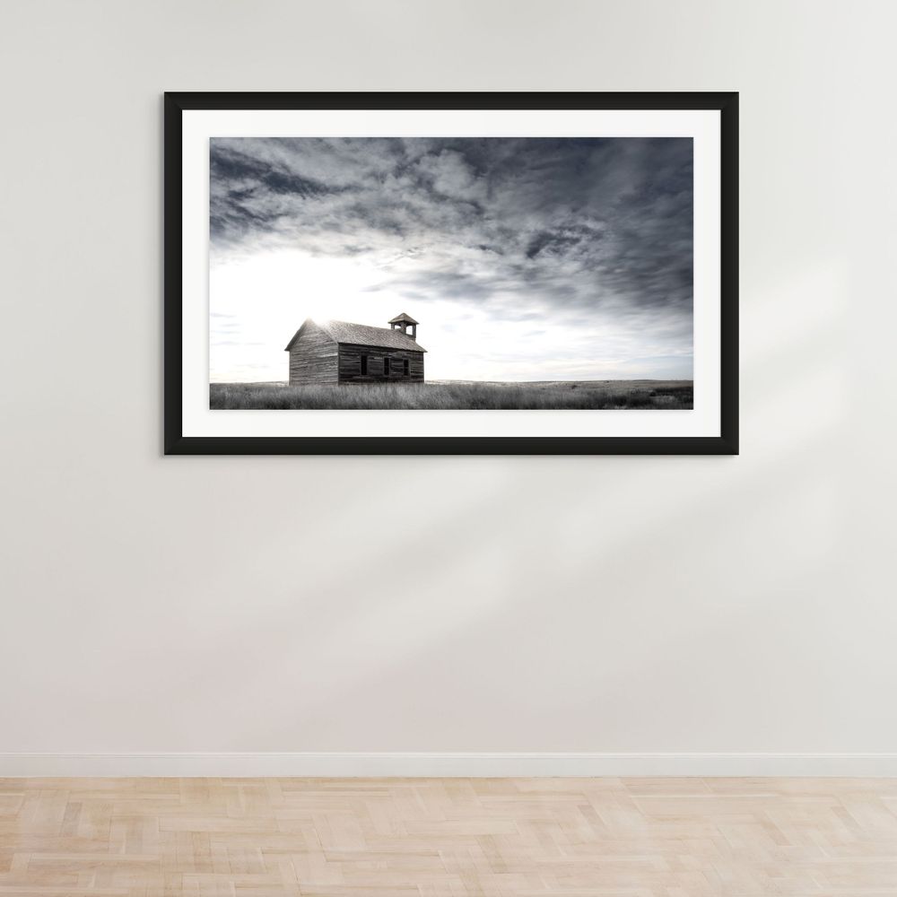 Minimalist black and white photograph of solitary schoolhouse on prairie horizon.