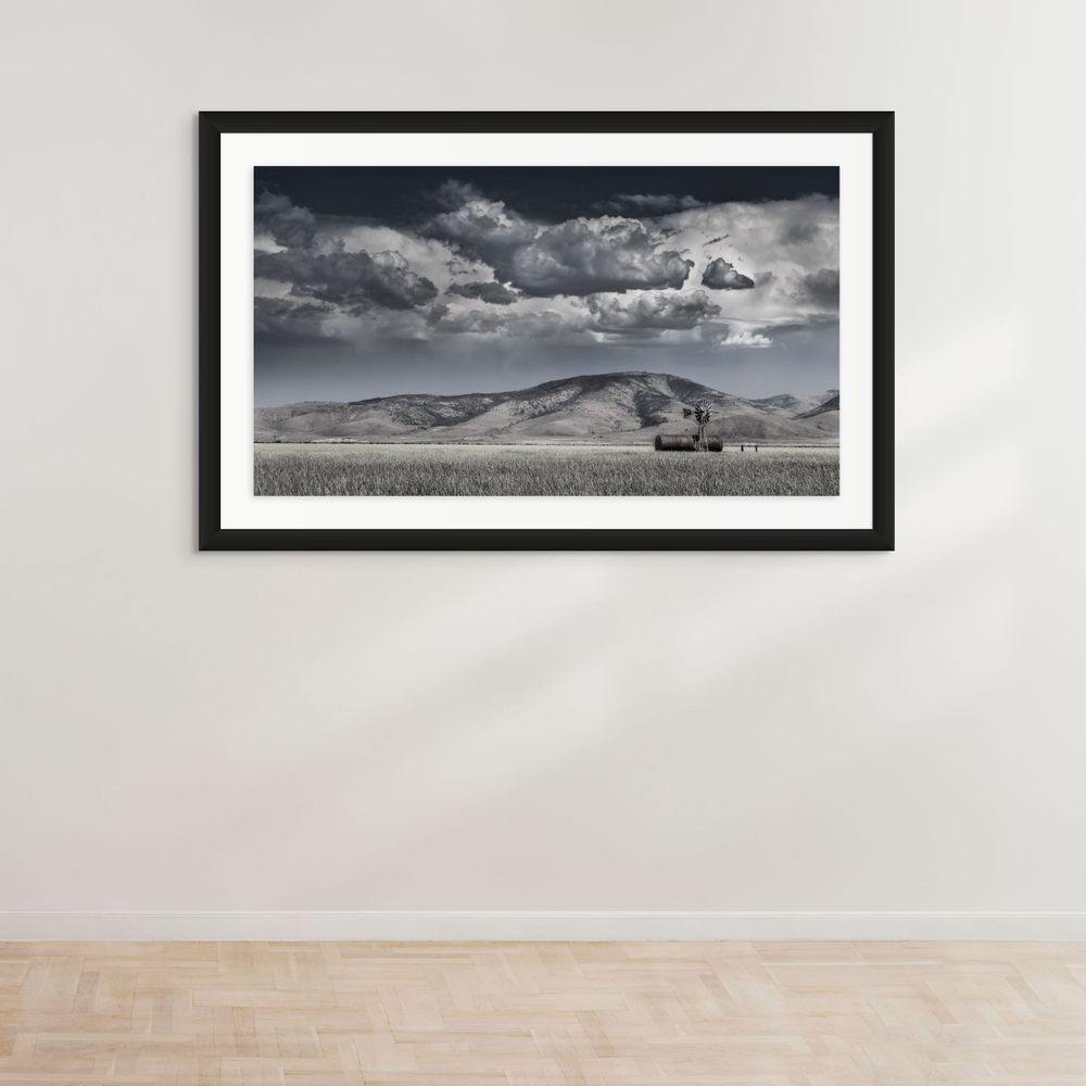 Old barn stands solitary against dramatic storm clouds rolling over rural mountain landscape.
