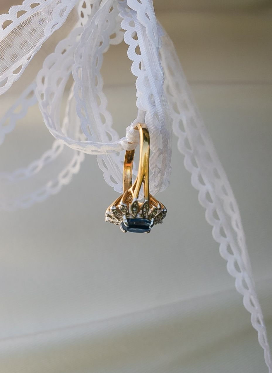 Gold wedding bands and blue sapphire engagement ring tied with white lace ribbon as a wedding detail shot.