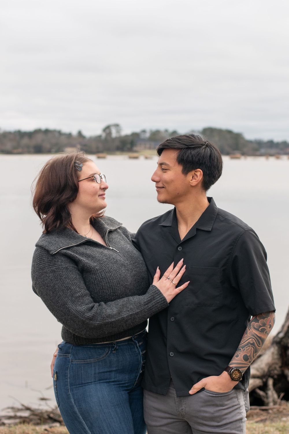 A couple shares a romantic moment together on a cloudy day at the beach, smiling and embracing each other.