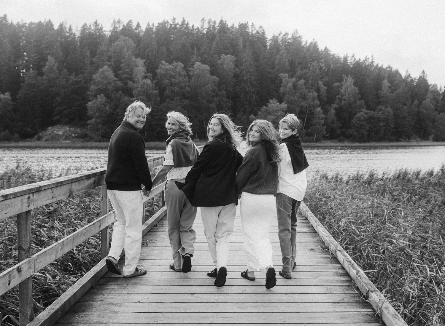 Group walking together on wooden boardwalk by lake with forest in background.