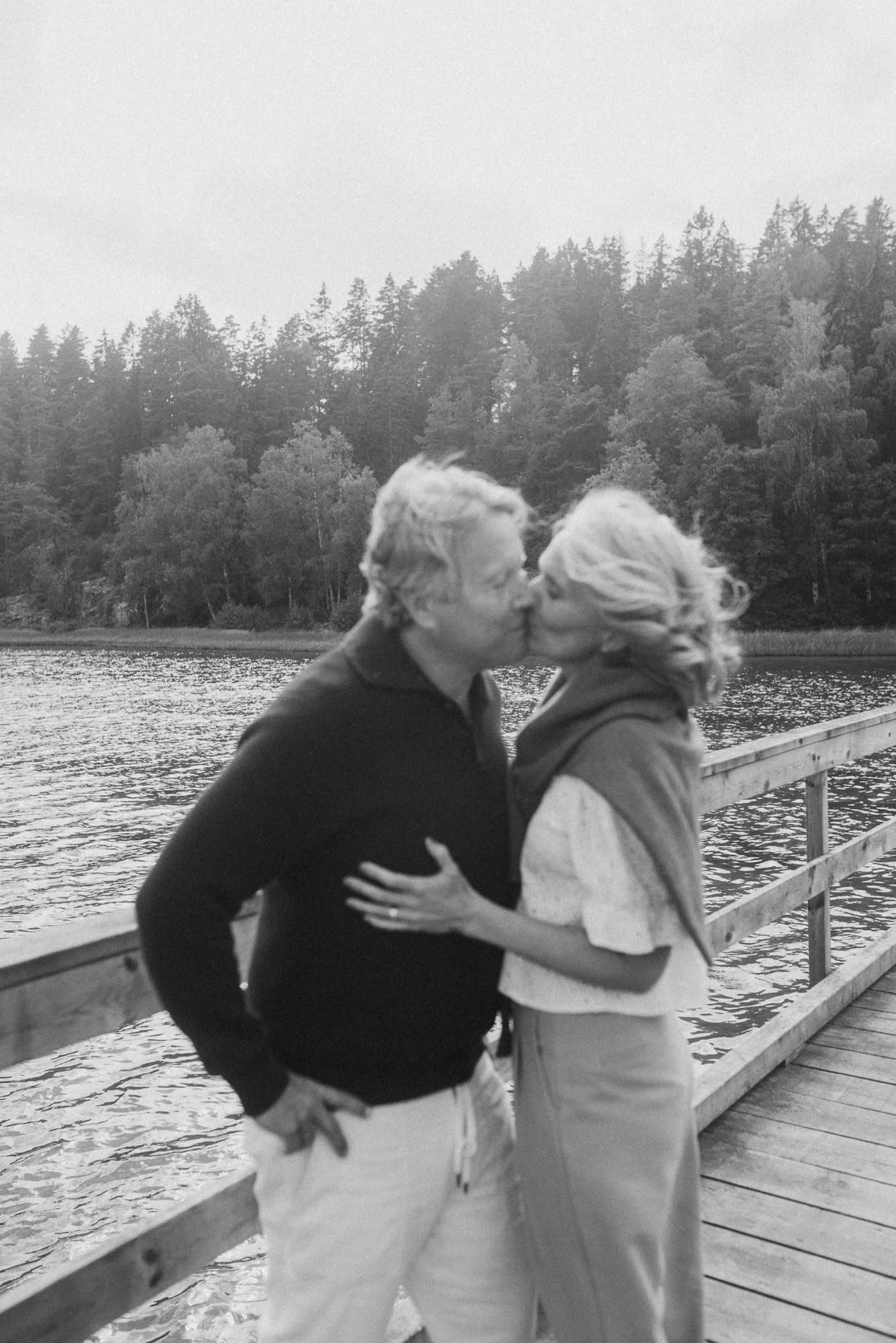 Romantic moment captured on wooden dock with pine forest and lake backdrop.