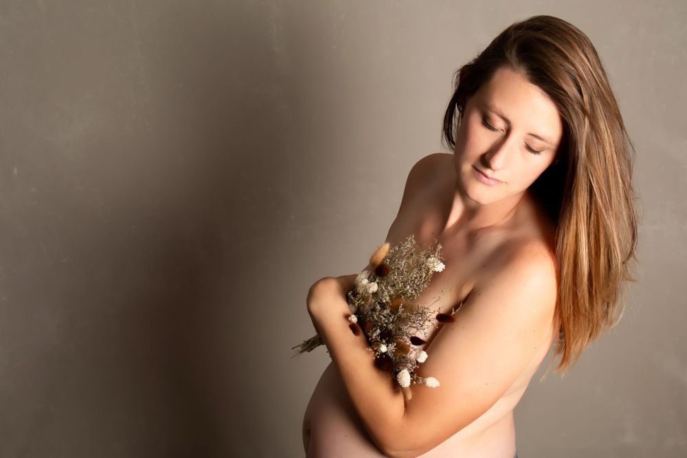 Artistic maternity portrait with small white flowers against neutral background in soft lighting.