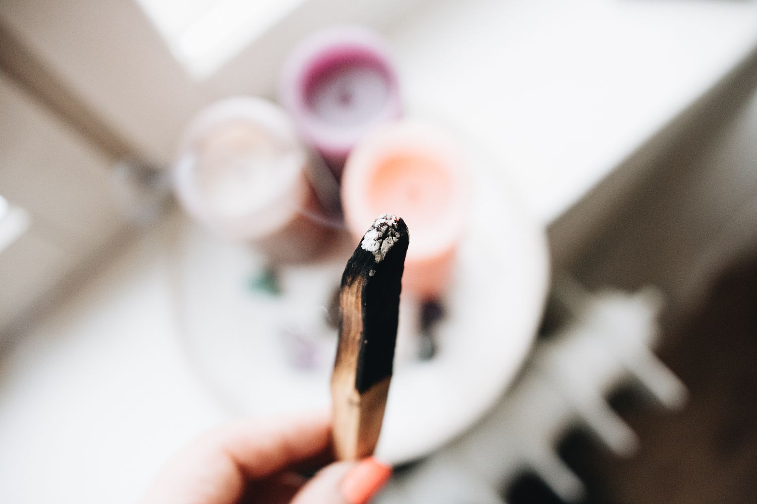 Black paintbrush held over a white palette with blurred colorful paint spots in the background.