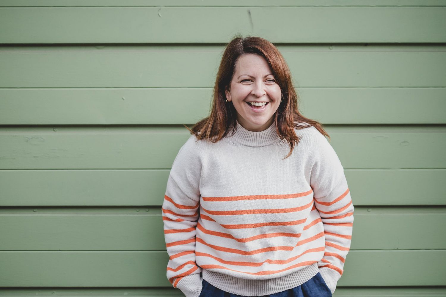 Person in striped turtleneck sweater smiling against green siding.