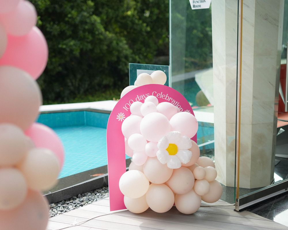 Pink and white balloon arch with daisy design next to pool at outdoor event.