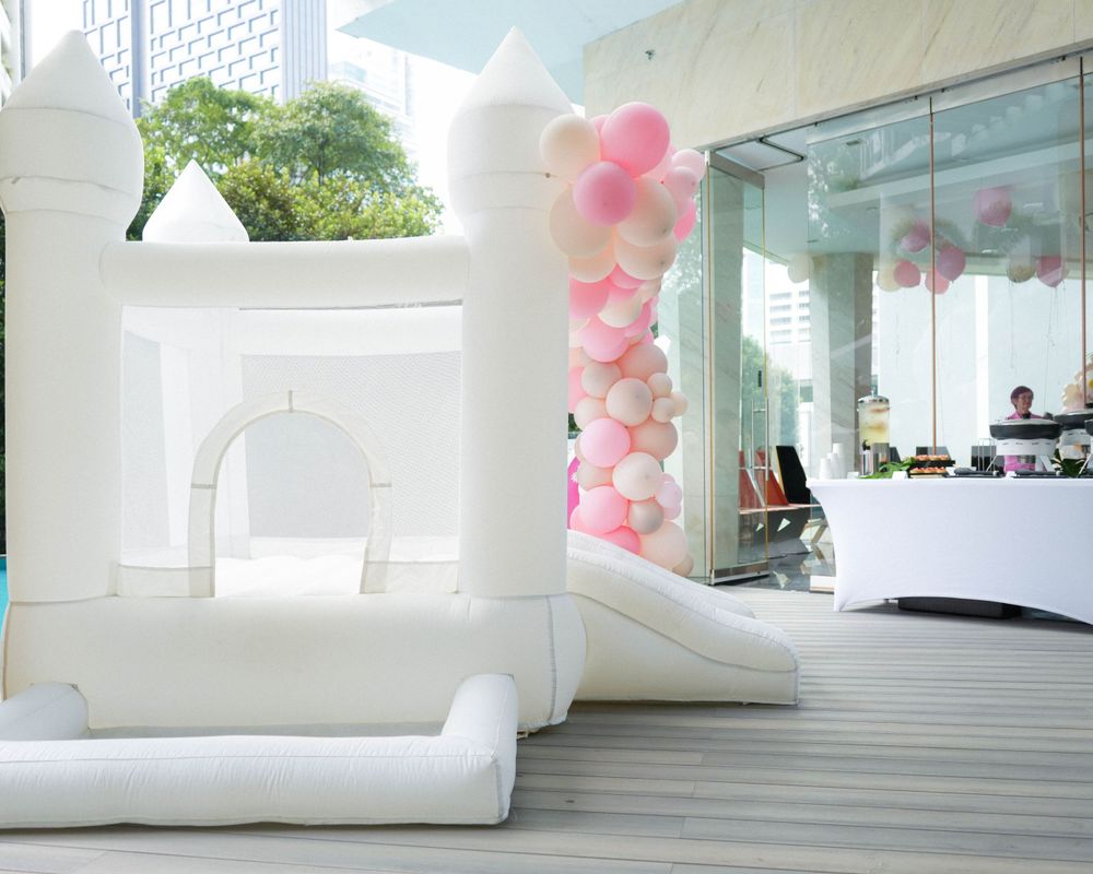 White bounce house installation with pink balloon arch decorations in a modern venue space.