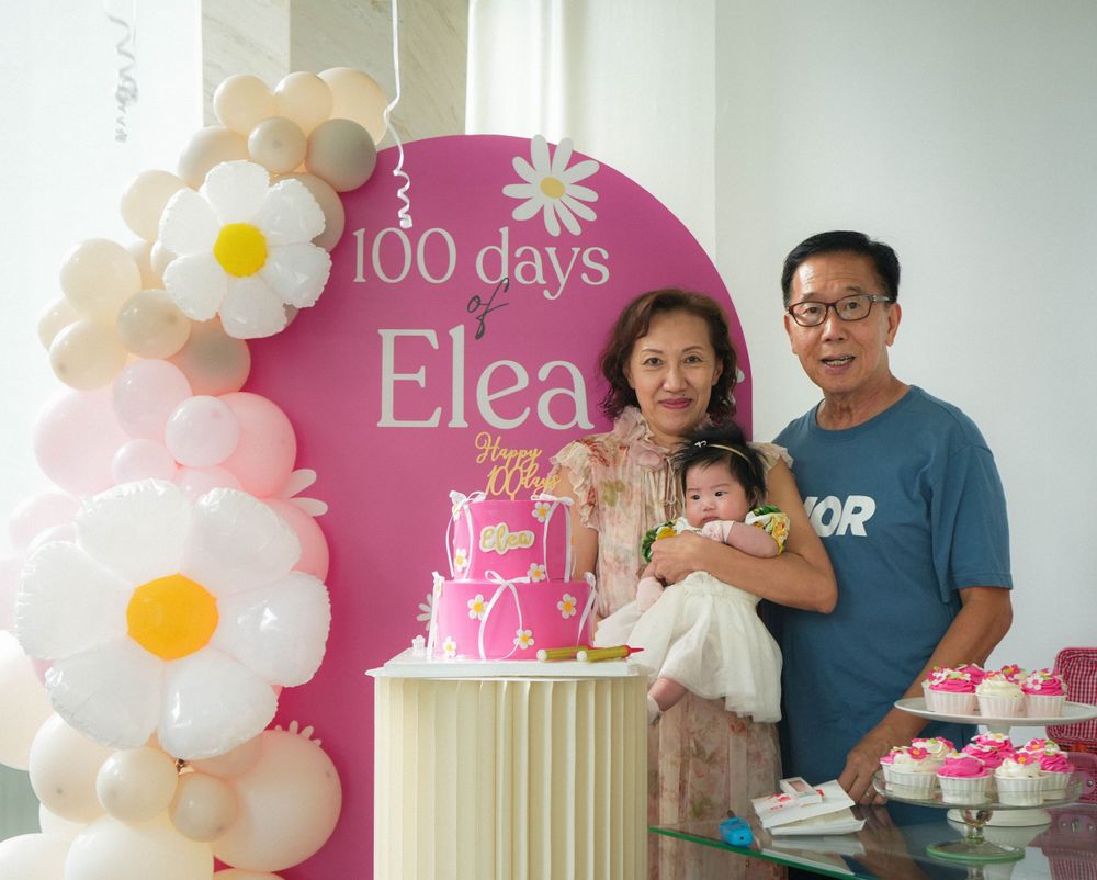 A 100 days celebration setup with pink backdrop and floral balloon decorations.