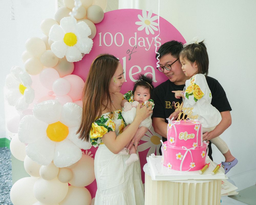 Family gathering at a 100 days celebration with balloon arch and pink cake.